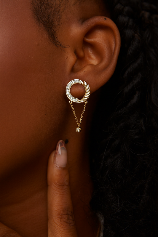 Close-up of a gold hoop earring with a chain detail worn by a person.
