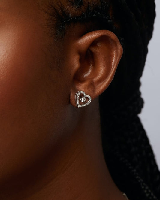 Heart-shaped earring worn by a person with braided hair against a neutral background