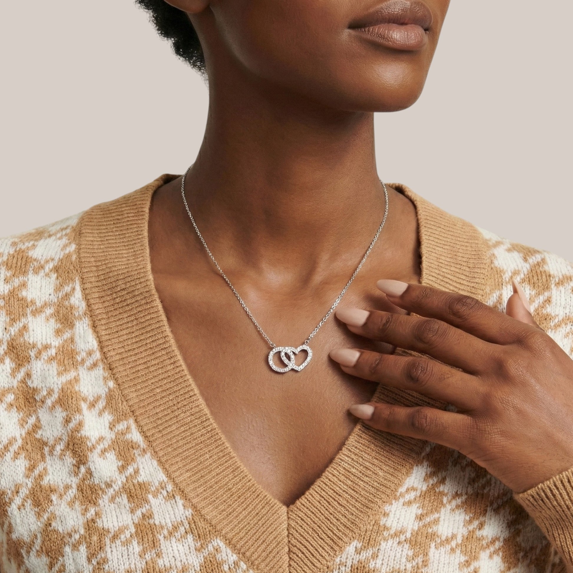Woman wearing a silver necklace with interlocking heart pendants, wearing a beige sweater.