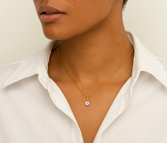 Woman wearing a gold necklace with a small round pendant against a neutral background