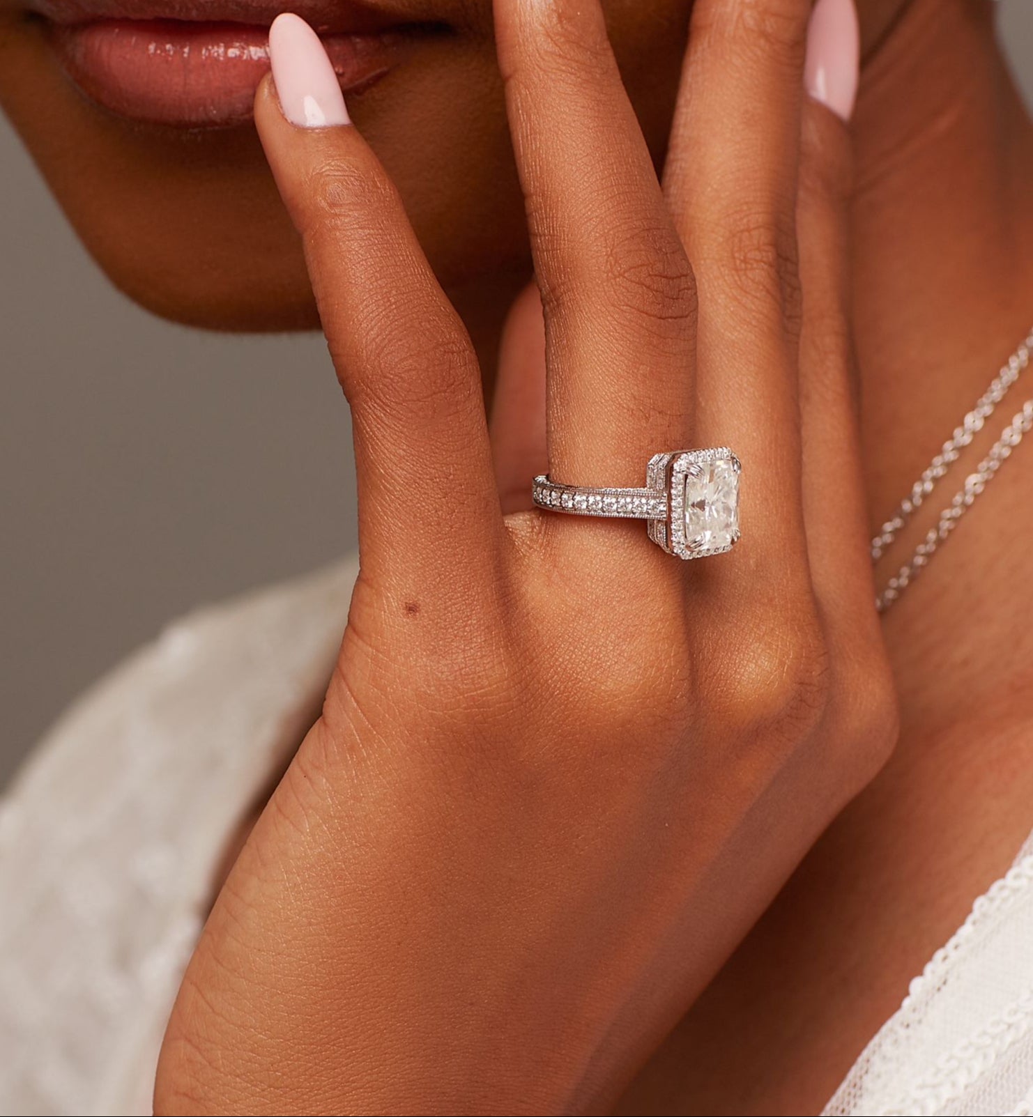 A person's hand displaying an 18 karat gold engagement ring with a moissanite gemstone on their finger.
