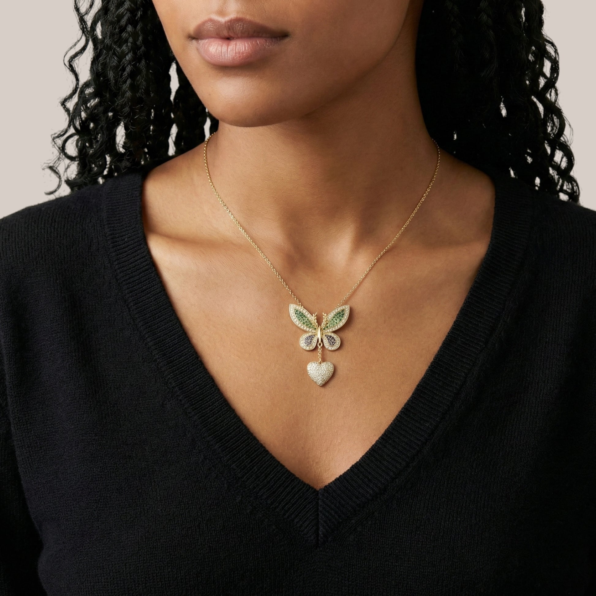 Woman wearing a butterfly and heart pendant necklace against a neutral background