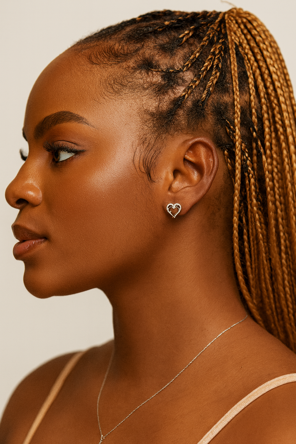Woman with braided hair wearing a heart-shaped earring and necklace on a neutral background