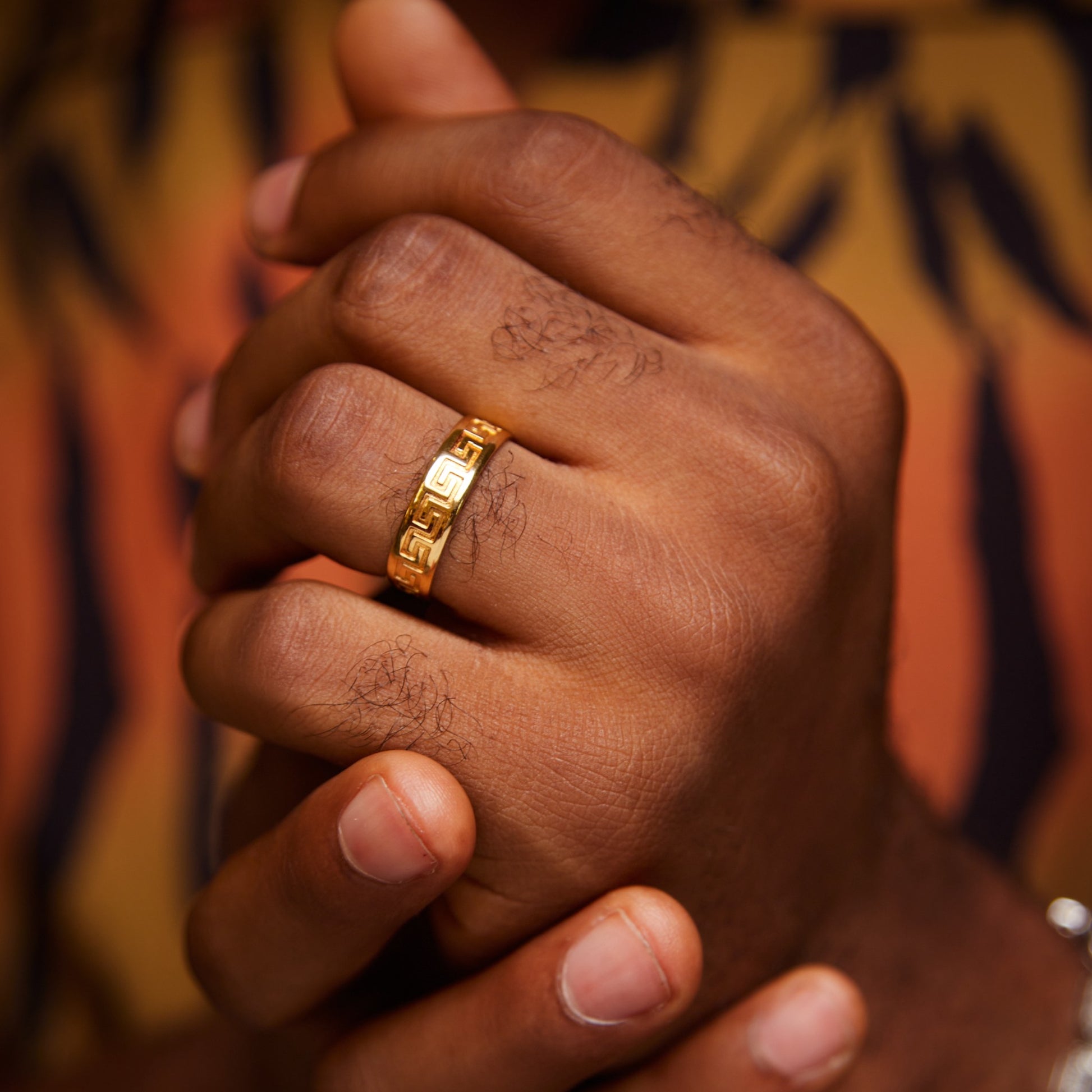 Close-up of a hand wearing a gold ring with a colorful patterned background