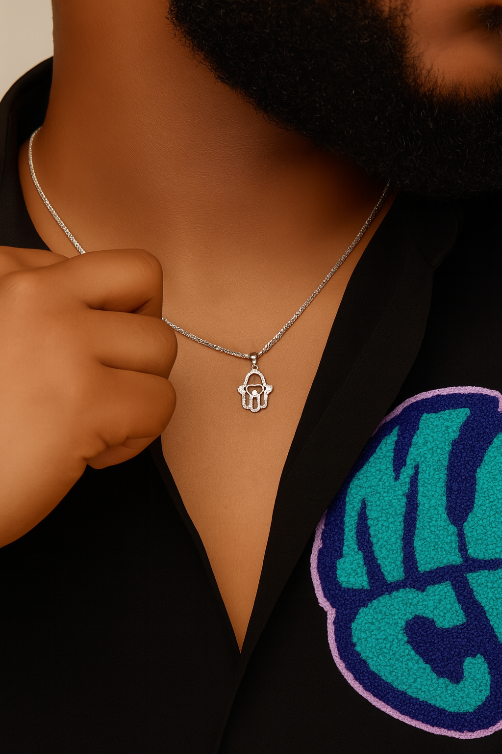 Person wearing a silver necklace with a hamsa pendant on a beige background