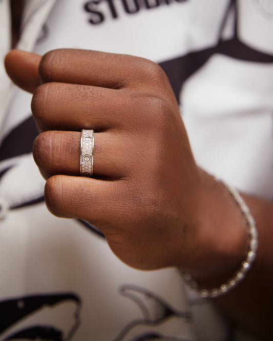 A man's hand holding a sterling silver band ring with a moissanite gemstone set in it.