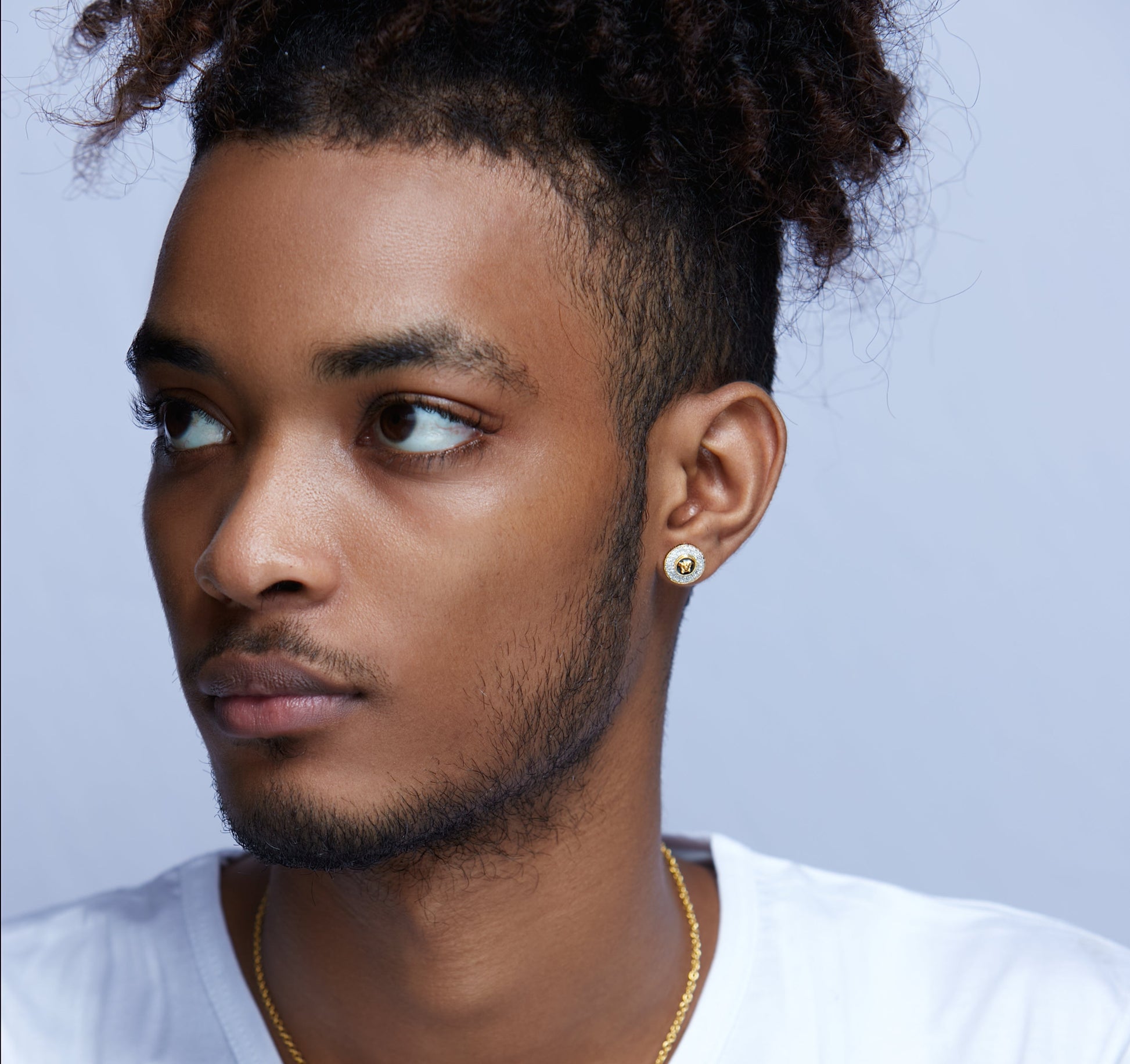 Man wearing a gold earring and necklace against a light purple background