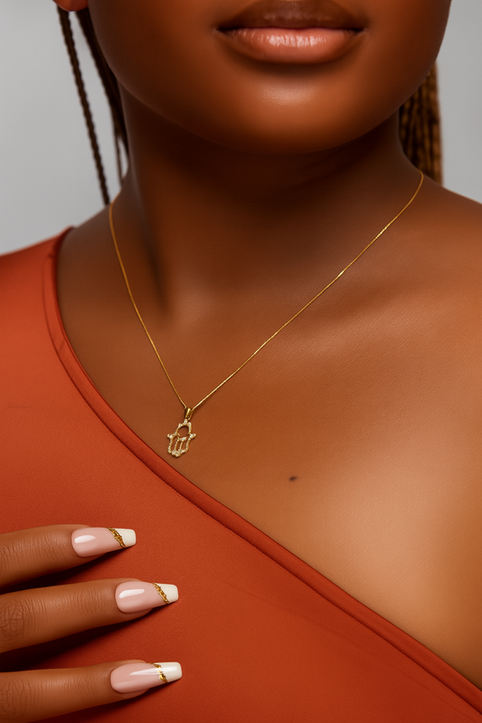 Close-up of a person wearing a gold necklace with a hamsa hand pendant.