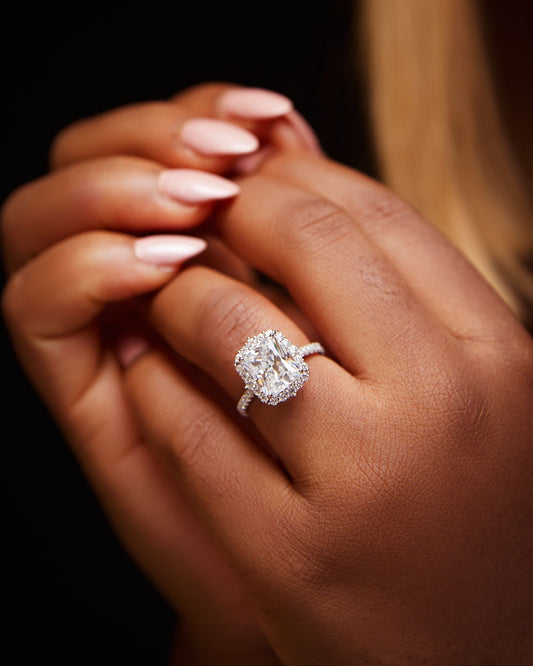 A person's hand holding a sterling silver engagement ring with a clear, polished band and a prominent, sparkling blue stone.