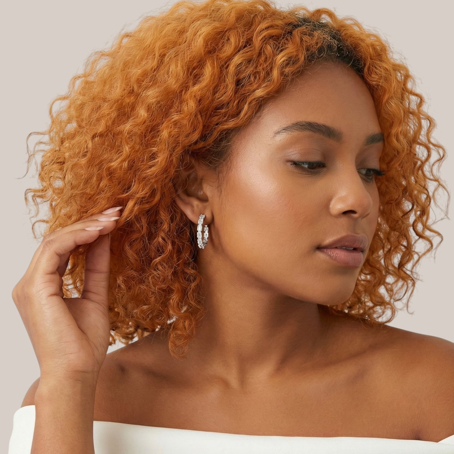 Woman with styled hair and earrings against a neutral background