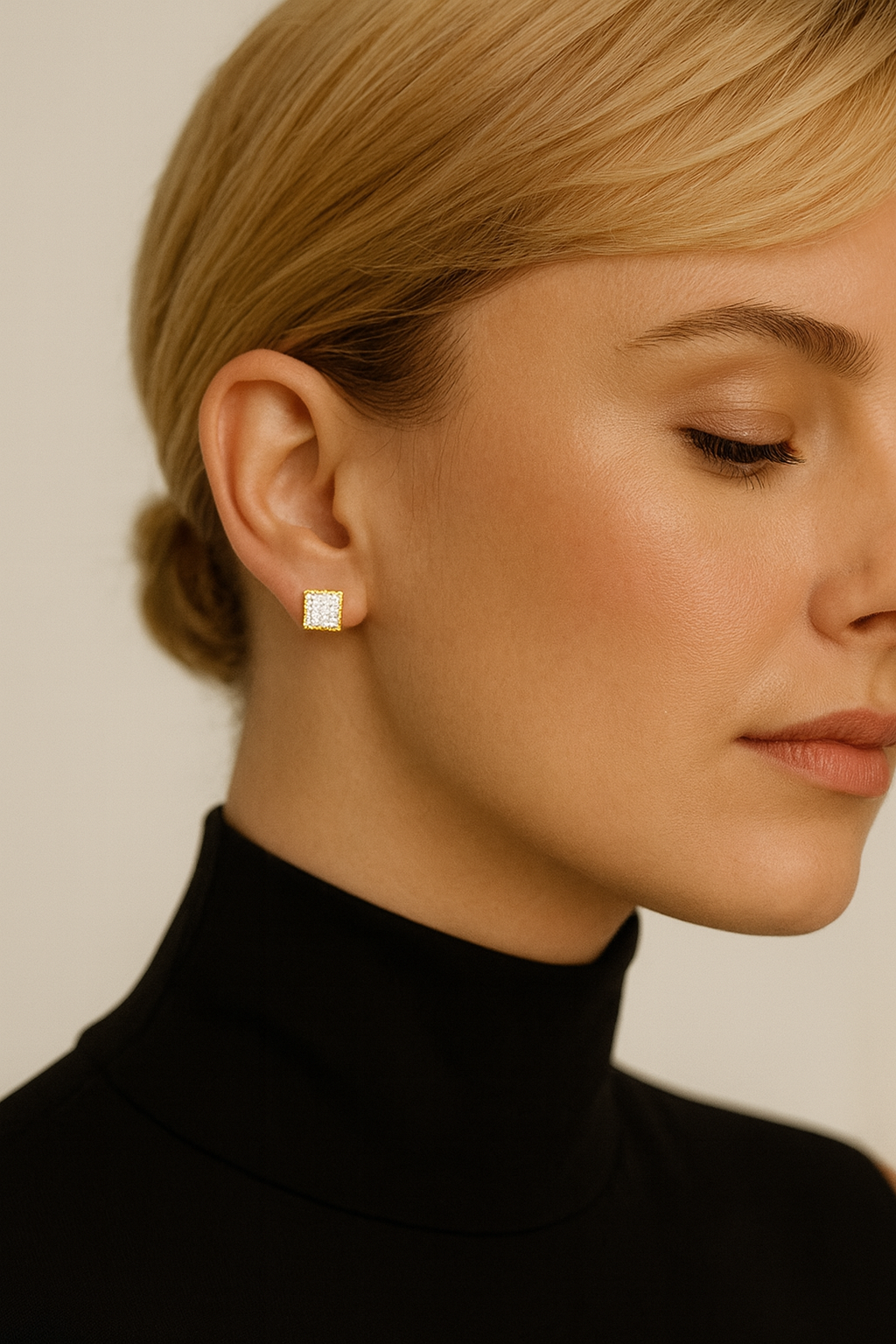 Close-up of a person wearing gold square stud earrings against a neutral background