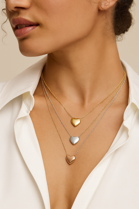 Close-up of a woman wearing three heart-shaped gold necklaces on a neutral background