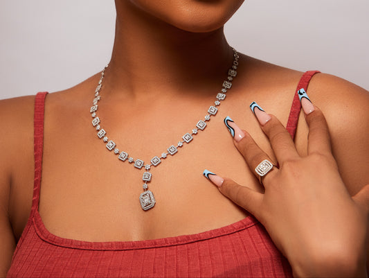 Woman wearing a diamond necklace, earrings, and ring against a neutral background