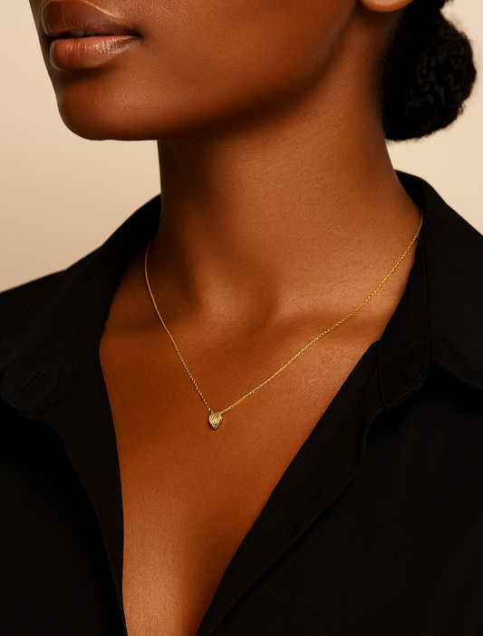 Close-up of a person wearing a gold necklace with a heart pendant on a beige background