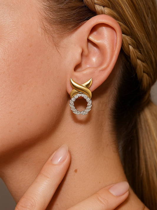 Gold and diamond earring worn by a person with braided hair.