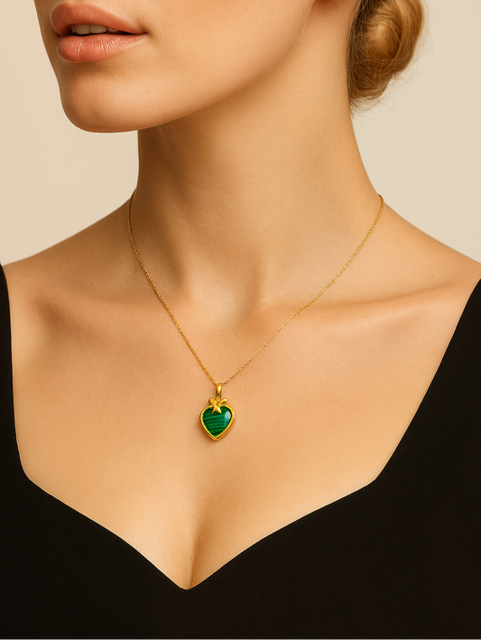 Woman wearing a gold necklace with a green heart pendant against a neutral background