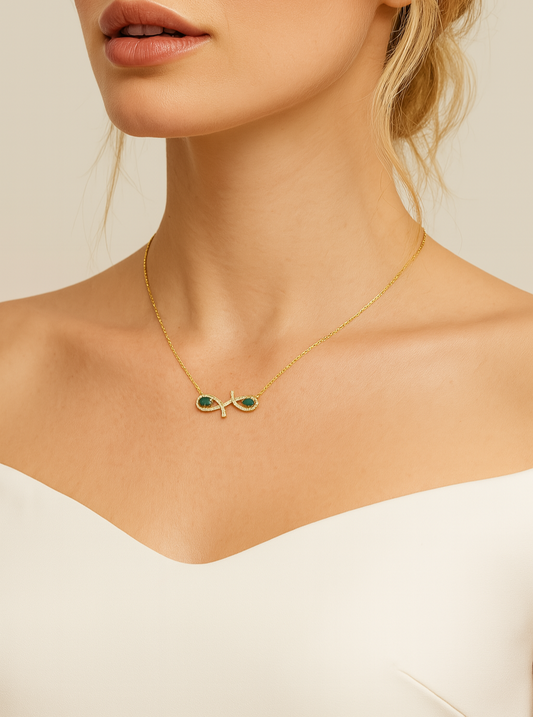 Close-up of a woman wearing a gold necklace with green gemstones on a beige background